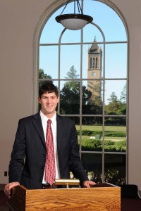 Headshot of Dakota Hoben at a podium inside the Memorial Union with the campanile in the background