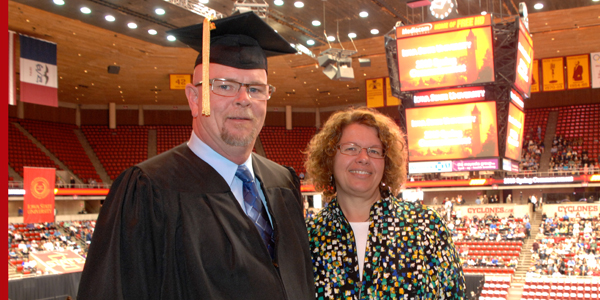 Gary High stands with his wife at commencement wearing a cap and gown.