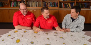 Jay Harmon, Steve Hoff, and Colin Johnson spread papers out on a table and analyze them