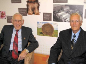 Wes Buchele who patented the first large round baler in 1966 with his graduate student Virgil Haverdink sit together at a museum with information about thier invention in the background