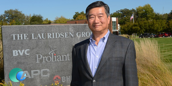Chia-Wei Chang stands in front of his company's sign with a building and lawn in the background