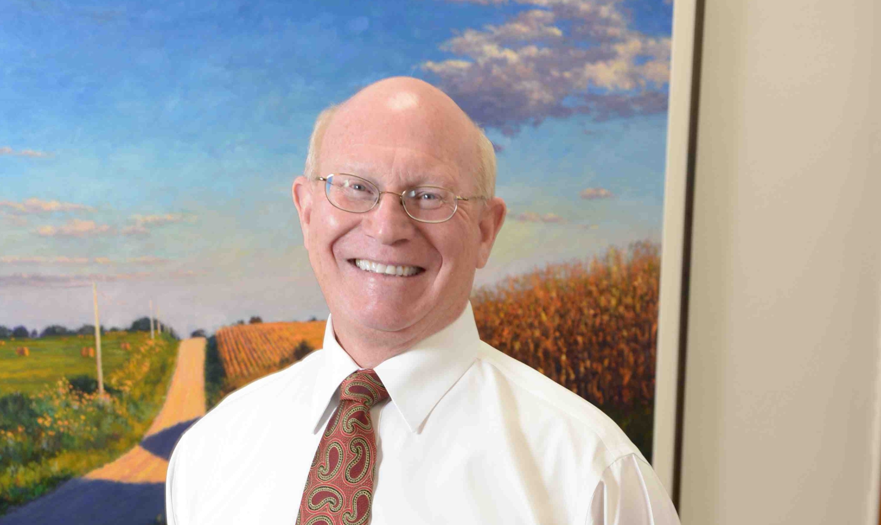 Headshot of Senior Associate Dean of CALS, Joe Colletti, with a painting of a rural countryside in the background
