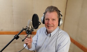 Professor Steve Mickelson sits near a microphone in a recording studio with headphones on and