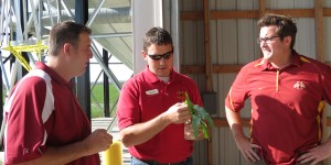 Agronomist Mark Licht analyzes an ear of corn while Brian and Jay Halbur talk with him