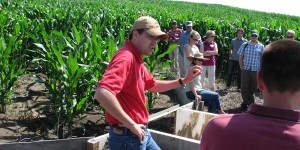 Matt Helmers talks to a group of people in a field of green corn
