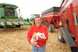 Scott Tapper holds a piglet in a field with machinery in the background