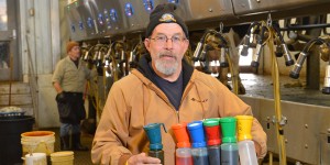 Dairy specialist Leo Timms holds different colored containers with a milking carasoul in the background