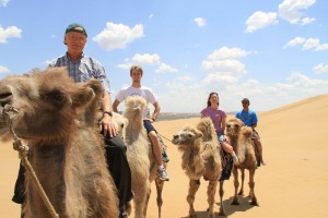 A Professor and students ride camels through a desert in China while on a study abroad.