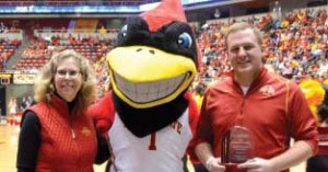 Dean Wintersteen stands with Cy and Jacob Thomson as she presents Jacob the Emerging Iowa Leader Award from the College of Agriculture and Life Sciences at center court in Hilton Coliseum.