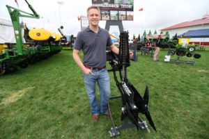 Colin Hurd stands next to his invention, TrackTill, at a farm show