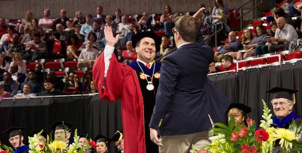 Brandon Hansen and Dean Robison high five as Brandon walks across the stage at convocation
