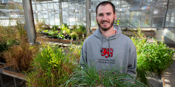 undergrad poses in greenhouse with grass plant