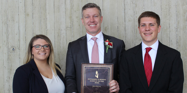 three business people stand together - center person is holding a plaque