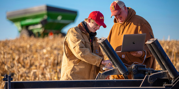 young farmer checks sensor technology with his father in a harvested corn field