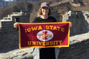 Betsy Freese holding an Iowa State University flag with the Great Wall of China in the background