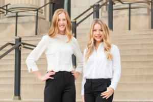 Megan Decker and Julia Campbell, each wearing white shirts and black pants, standing on cement steps.