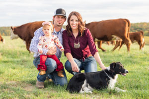 Amos and Tina Troester kneeling, holding their daughter, with cattle in the background.