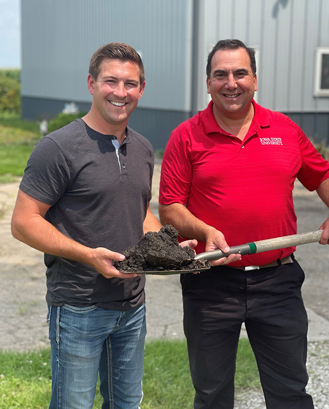 Mitchell Hora and Daniel J Robison holding a shovel with soil on it